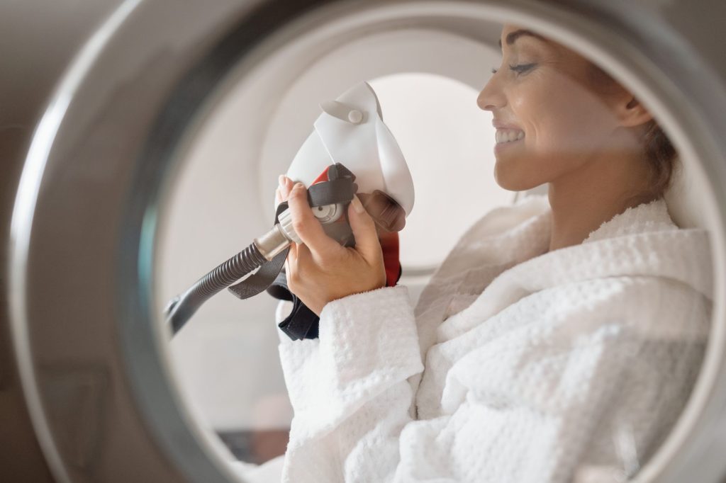 Woman in white robe putting mask on for hyperbaric therapy